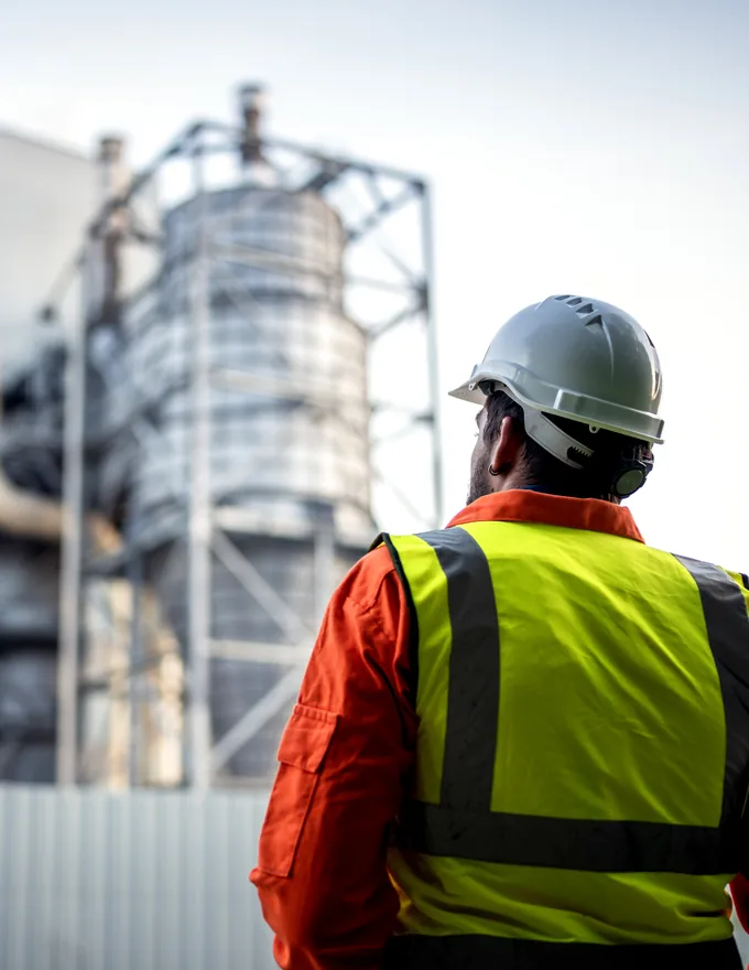 Site worker in a high-visibility vest looking towards an industrial plant