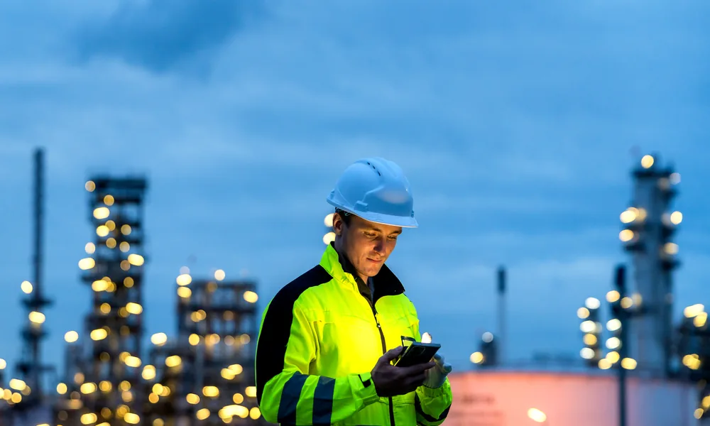 Engineer in a hard hat checking a device at an industrial plant at dusk