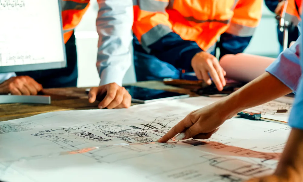 Engineers in high-visibility jackets reviewing technical drawings